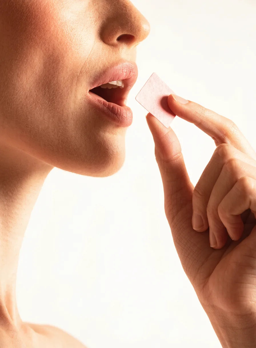 A woman preparing to place a pale rose Tabb oral strip on her tongue